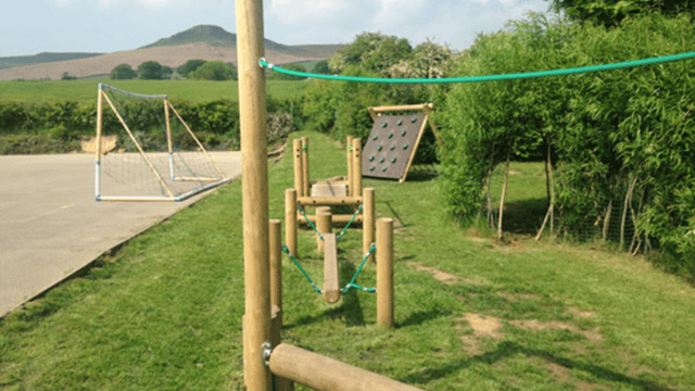 Field with climbing frame and a playground to the left with a football net