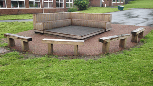 Decking area built from wood on a field within the school grounds with benches surrounding