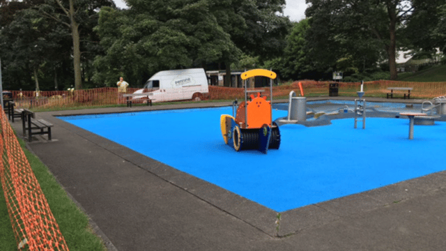 Blue tarmac area with playground being installed on it