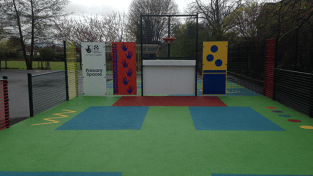 School playground with different coloured squares on the tarmac with games on and fencing surrounding it